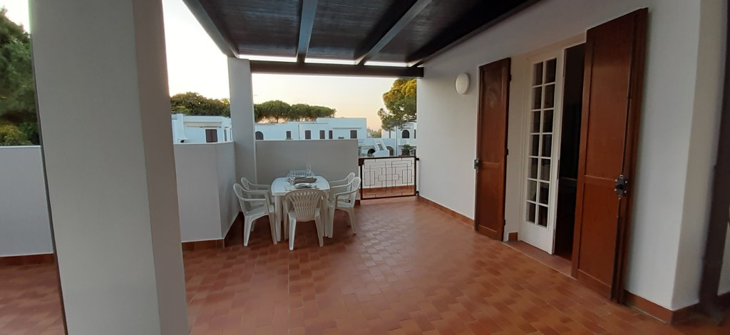 Ampia terrazza con tavolo e sedie, vista sul verde circostante, all'interno di una villetta nel residence 'Alla vigna'.