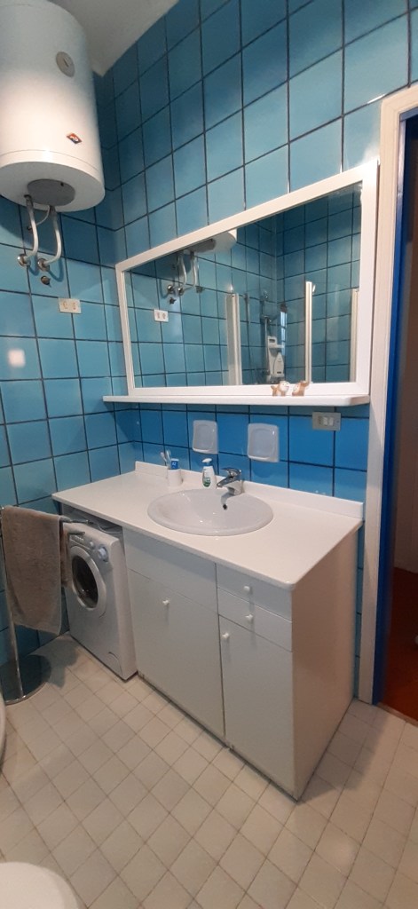 Bathroom featuring blue tiled walls, a white sink with mirror, a washing machine, and adequate storage space.