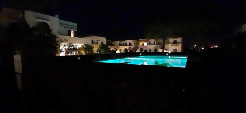 Night view of a villa complex with illuminated swimming pools surrounded by greenery.