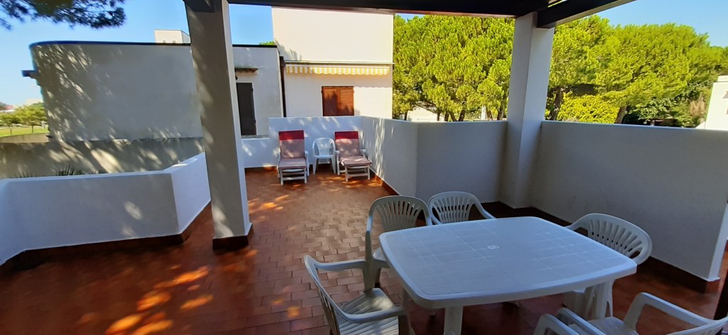 Ampia terrazza esclusiva di una villetta, con tavolo e sedie bianche,sdraio e vista su un paesaggio verdeggiante.