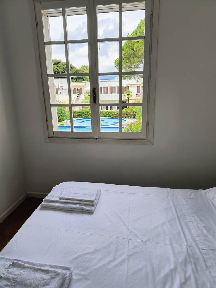 Blick aus einem Schlafzimmerfenster auf die Außenansicht der Villa mit einem Pool und grünem Garten.